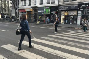 Une femme non-voyante traverse la rue après avoir activé les feux sonores du passage piéton